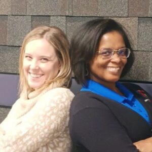 Two women standing back to back and smiling at camera